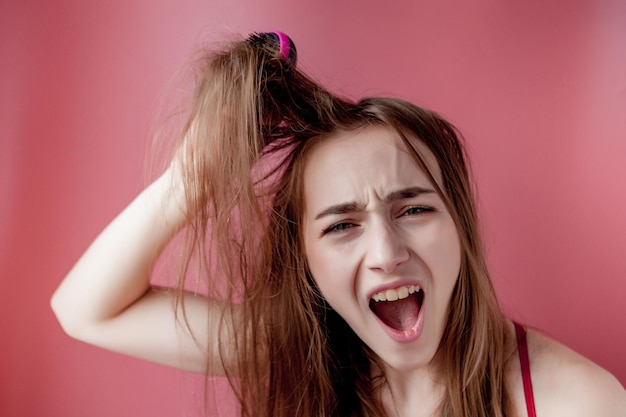 Zdjęcie młoda piękna dziewczyna ma problemy podczas gdy włosy na różowym tle