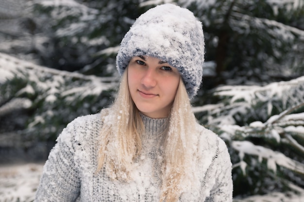 Młoda piękna dziewczyna o długich białych włosach gra śnieżkami. Dobrze się bawi, rzuca śniegiem i raduje się śniegiem. Zimowy spacer na zewnątrz.