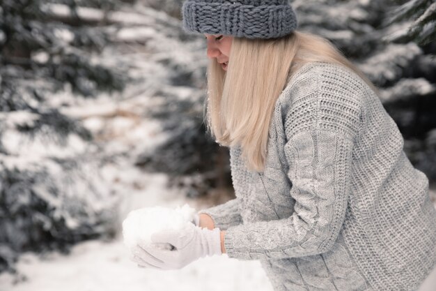 Młoda piękna dziewczyna o długich białych włosach gra śnieżkami. Dobrze się bawi, rzuca śniegiem i raduje się śniegiem. Zimowy spacer na zewnątrz.