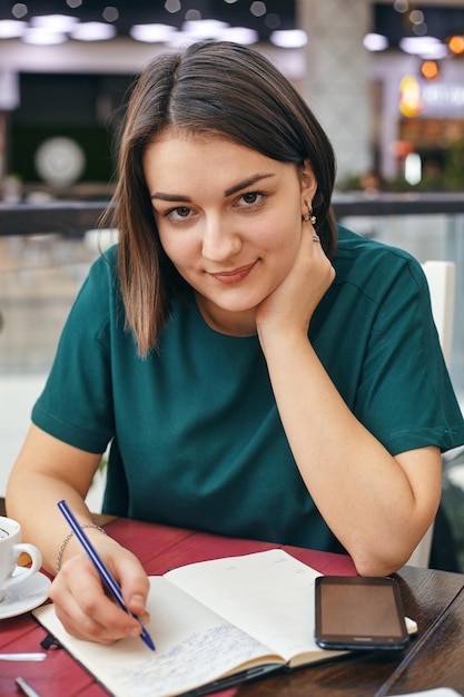 Młoda piękna dziewczyna pisze coś w swoim notesie siedząc w biurze.