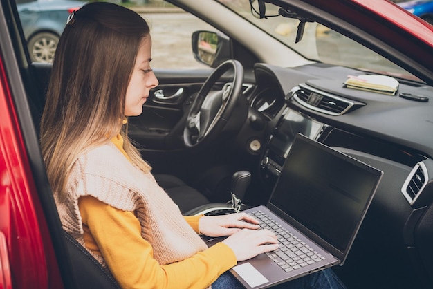 Młoda piękna dziewczyna pracuje na laptopie siedząc w samochodzie freelancer bloger w pracy praca zdalna nowoczesne technologie