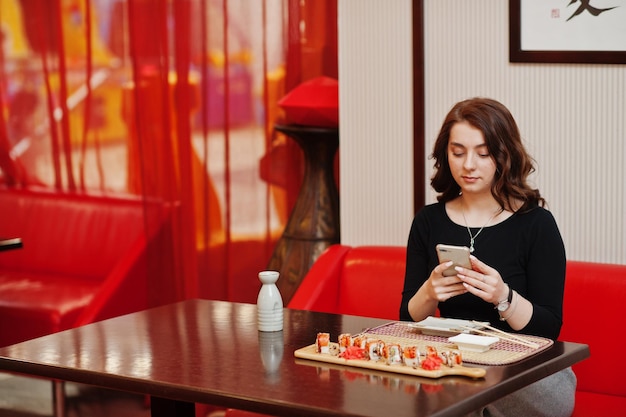 Młoda Piękna Dziewczyna Robi Zdjęcie Przez Telefon Sushi W Tradycyjnej Japońskiej Restauracji