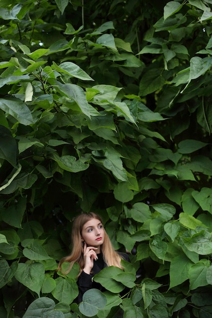 Młoda piękna dziewczyna stoi przy ścianie liści