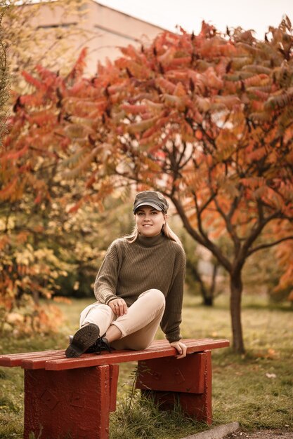 Młoda piękna dziewczyna ubrana w stylowe ubrania, zielony sweter i beżowe spodnie, w jesiennym parku z pięknymi drzewami