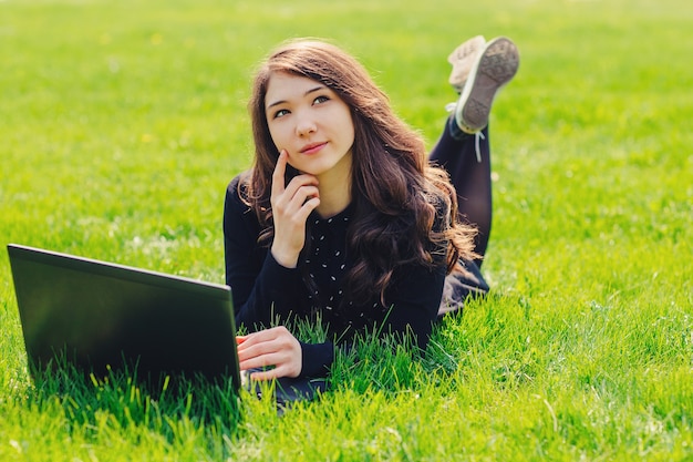 Młoda piękna dziewczyna, uczennice za pomocą laptopa w parku, leżąc na zielonej trawie. Pojęcie czasu wolnego. Koncepcja e-learningu.