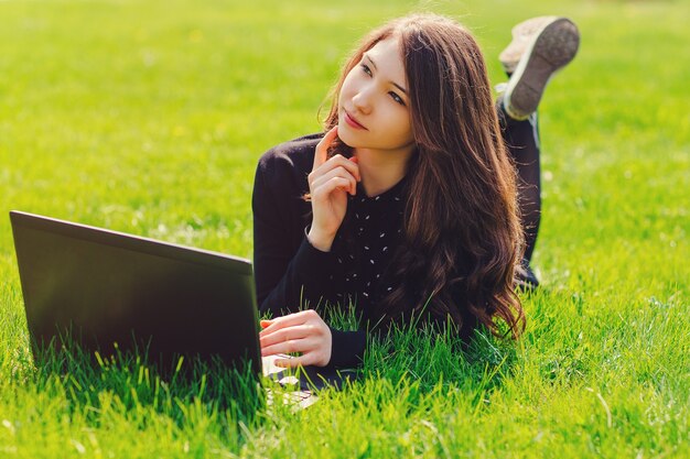 Młoda piękna dziewczyna, uczennice za pomocą laptopa w parku, leżąc na zielonej trawie. Pojęcie czasu wolnego. Koncepcja e-learningu.