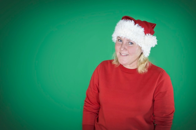 Młoda piękna dziewczyna w Boże Narodzenie Santa kapelusz na pojedyncze zielone tło z szczęśliwą twarzą stojącą i uśmiechniętą z pewnym uśmiechem.