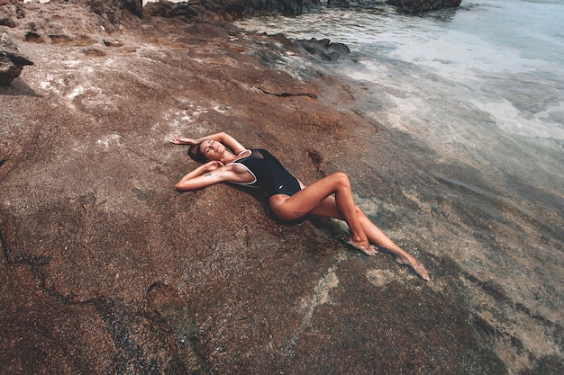 Młoda piękna dziewczyna w czarnym zamkniętym stroju kąpielowym relaksuje się i opala na plaży w Tajlandii w Phuket