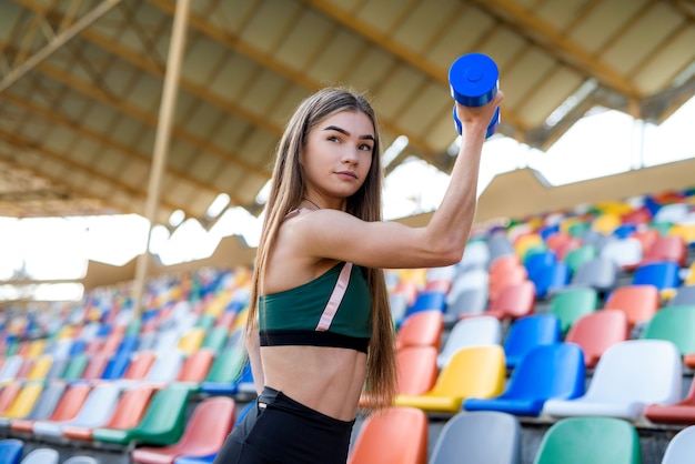 Młoda piękna dziewczyna w sportowej pracy z hantlami na stadionie miejskim w lecie. Koncepcja sportu