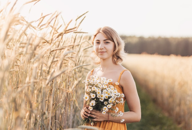 Młoda piękna dziewczyna z bukietem stokrotek na polu pszenicy