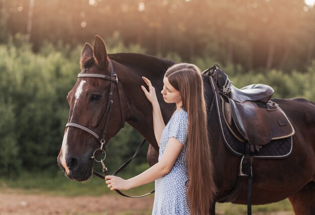 Młoda piękna dziewczyna z długimi włosami głaszcze konia i patrzy na nią latem na łonie natury.