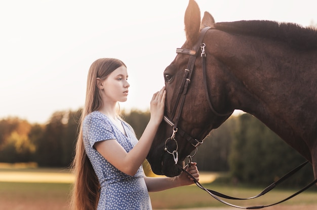 Młoda piękna dziewczyna z długimi włosami i brązowym koniem patrzą na siebie.