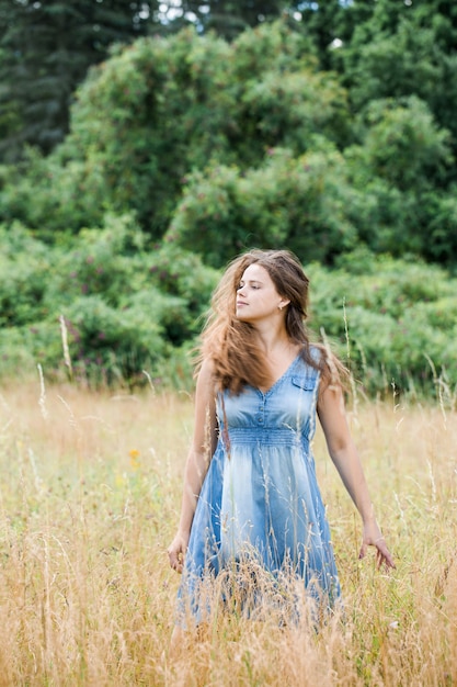 Młoda piękna dziewczyna z pięknymi długimi włosami w niebieskiej sukience spaceruje po polu