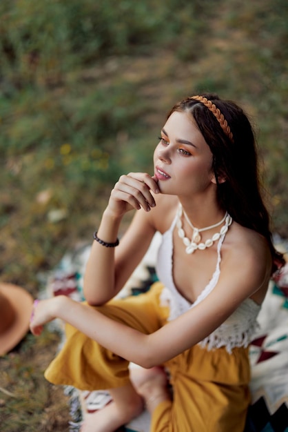 Młoda piękna hipis kobieta siedzi na ziemi w przyrodzie jesienią w eko-odzieży w świetle zachodzącego słońca styl życia podróży i harmonii ze światem