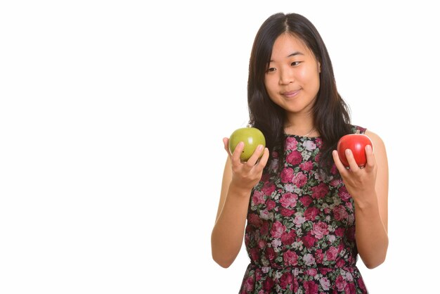 Młoda piękna kobieta Azji, wybierając między zielonym i czerwonym jabłkiem na białym tle