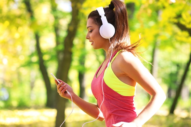 Młoda piękna kobieta biegająca w jesiennym parku i słuchająca muzyki przez słuchawki