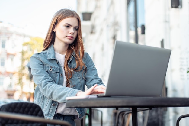 Młoda piękna kobieta freelancer za pomocą laptopa siedząc przy stole w kawiarni na świeżym powietrzu