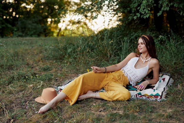 Młoda piękna kobieta hipis leżąca na ziemi w przyrodzie jesienią w eko ubraniach w żółtych spodniach w świetle zachodzącego słońca