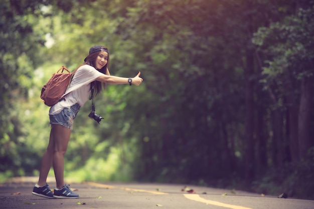 Młoda piękna kobieta hitchhiking pozycję na drodze.