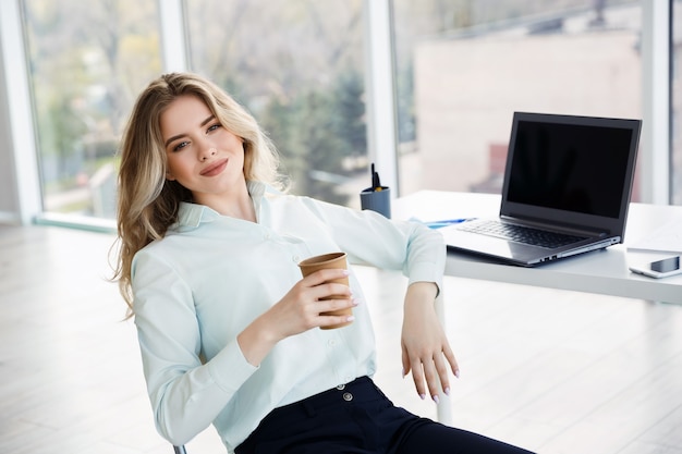 Młoda piękna kobieta pije kawę podczas przerwy w biurze. Koncepcja relaksu