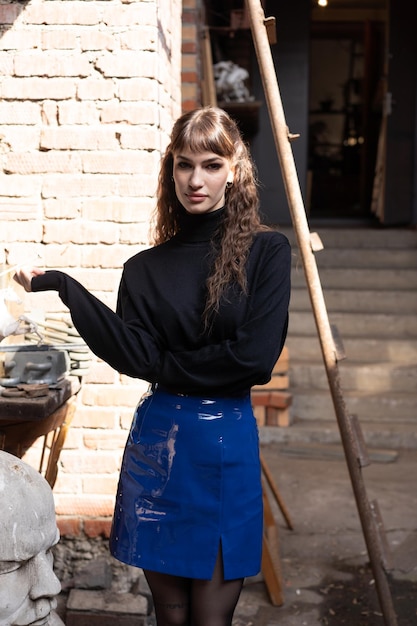 Zdjęcie młoda piękna kobieta pozuje w czarnym swetrze na zewnątrz i niebieskiej spódnicy stojącej w warsztacie
