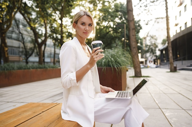 Młoda piękna kobieta pracuje na laptopie siedząc na ławce na ulicy