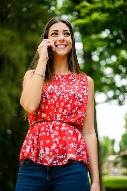 Młoda piękna kobieta rozmawia przez telefon w parku