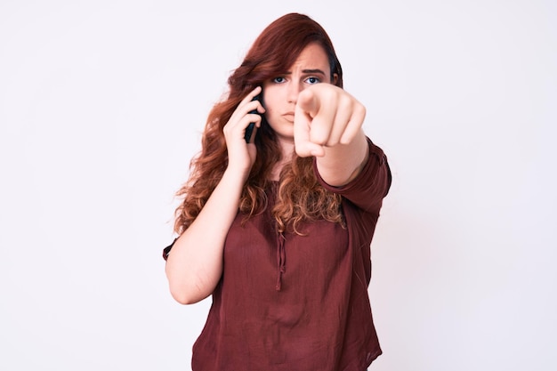 Zdjęcie młoda piękna kobieta rozmawiająca na smartfonie, wskazująca palcem na kamerę i pewny siebie gest wyglądający poważnie