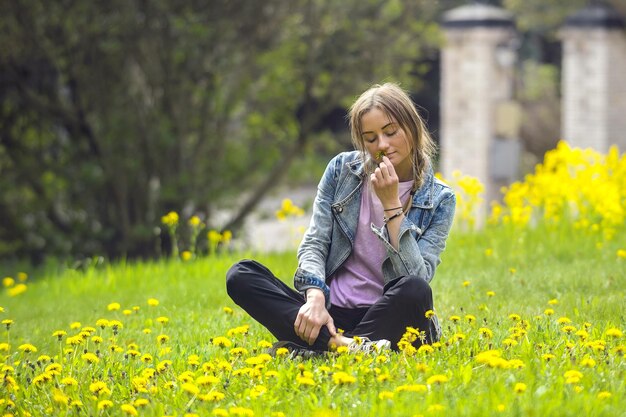 młoda piękna kobieta siedzi na jasnozielonej łące z żółtymi kwiatami