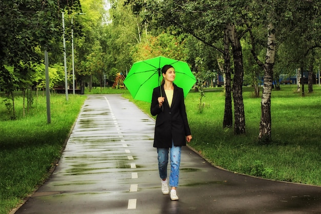 Młoda piękna kobieta spaceru pod zielonym parasolem