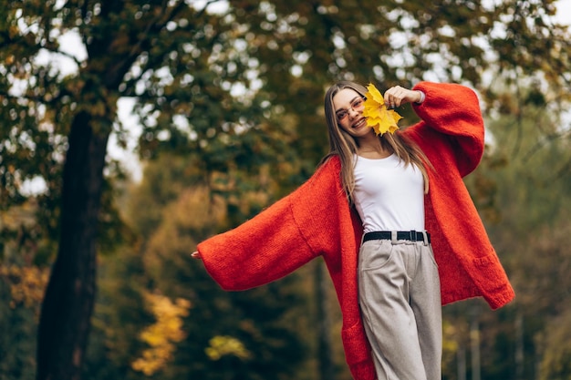 Młoda piękna kobieta spacerująca w jesiennym parku i trzymająca liście