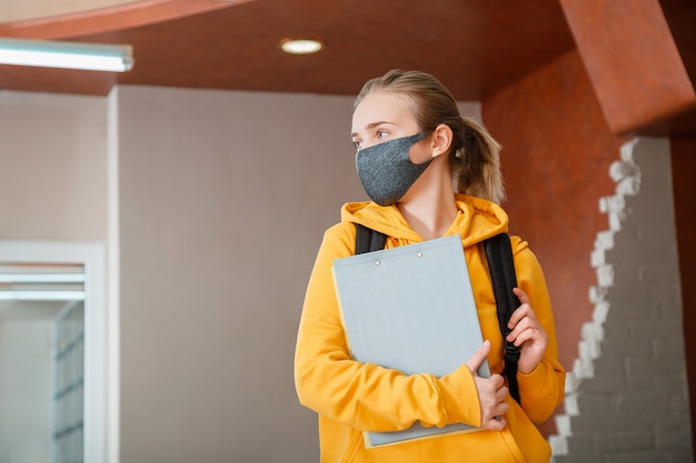 Młoda piękna kobieta studentka nosząca maskę ochronną z plecakiem nastoletnia dziewczyna blondynka kaukaski nastolatek podróżnik w masce trzymający zeszyty szczęśliwy student w ponownym otwarciu kampusu uniwersyteckiego covid lockdown
