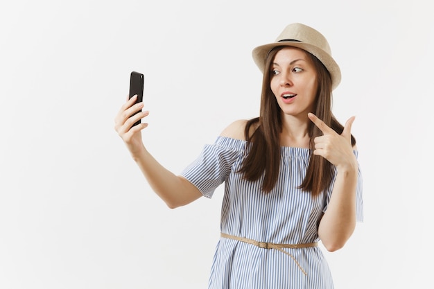 Młoda piękna kobieta ubrana w niebieską sukienkę, kapelusz robi selfie strzał na telefon komórkowy lub rozmowy wideo na białym tle. Ludzie, szczere emocje, koncepcja stylu życia. Powierzchnia reklamowa. Skopiuj miejsce.