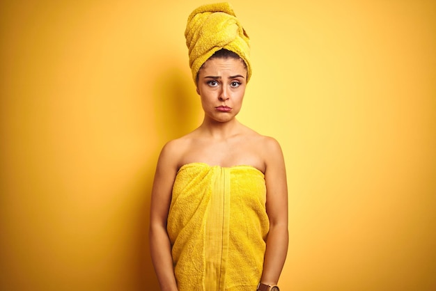 Młoda piękna kobieta ubrana w ręcznik po prysznicu na odizolowanym żółtym tle przygnębiona i zmartwiona płaczem zły i przestraszony Smutny wyraz twarzy