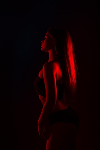 Młoda piękna kobieta w bieliźnie pozuje w czerwonym świetle z tyłu