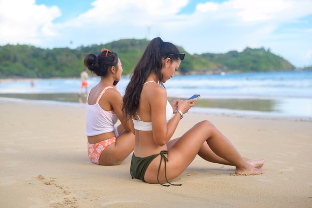 Młoda piękna kobieta w Bikini słuchając muzyki i używając smartfona na plaży