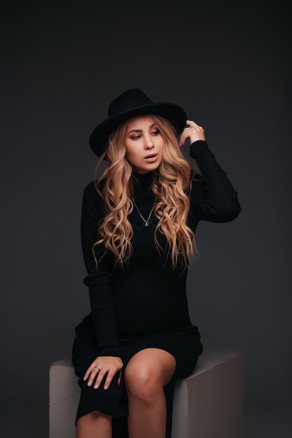 Zdjęcie młoda piękna kobieta w czarnym kapeluszu siedzi na czarnej ścianie
