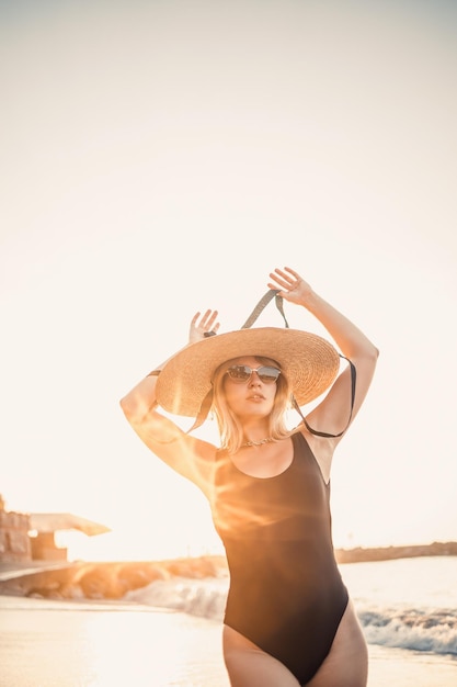 Młoda piękna kobieta w czarnym stroju kąpielowym i kapeluszu w okularach spacery po plaży w Turcji o zachodzie słońca Koncepcja rekreacji na morzu Selektywna ostrość