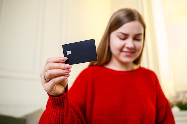 Młoda Piękna Kobieta W Czerwonym Swetrze Trzyma Kartę Bankową. Karta Kredytowa Do Zakupów Online. Selektywne Skupienie