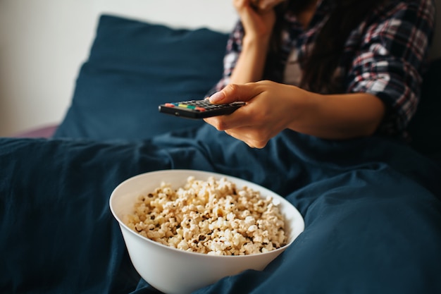 Młoda Piękna Kobieta W Ranku łóżku W Domu. Trzymaj Pilota I Oglądaj Telewizję Lub Film. Miska Z Popcornem Na łóżku. Wytnij Widok I Zamknij.