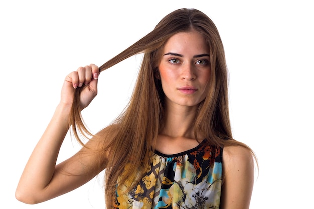 Młoda piękna kobieta w różnokolorowej bluzce z długimi kasztanowymi włosami trzymającymi kosmyk włosów