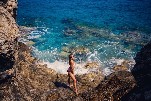 Młoda piękna kobieta w stroju kąpielowym stoi na kamienistej plaży Morza Śródziemnego Koncepcja morskiej rekreacji Selektywne skupienie
