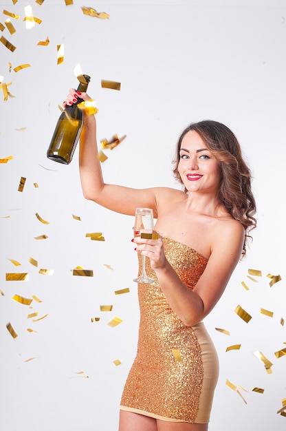 Młoda piękna kobieta w złotej sukni pije szampana, bawiąc się na imprezie ze złotym konfetti na białym tle