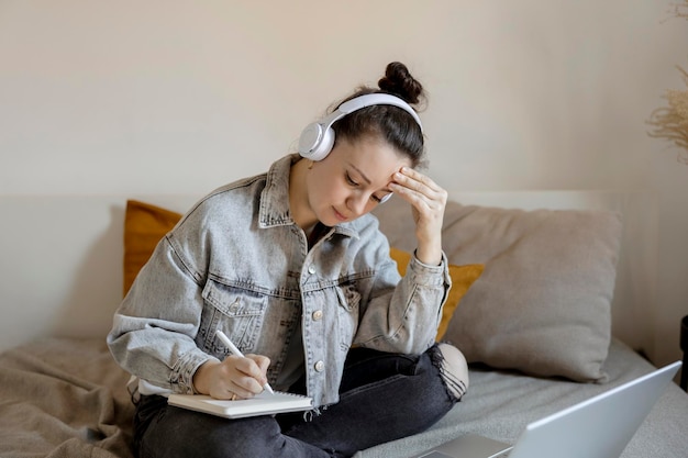 Młoda piękna kobieta w zwykłych ubraniach siedzi na łóżku w domu z laptopem i studiuje Dziewczyna korzystająca z platformy e-learningowej do nawiązania połączenia wideo z nauczycielem Kształcenie na odległość