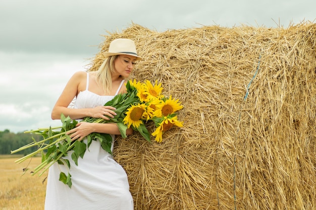 Młoda piękna kobieta z bukietem słoneczników na polu w pobliżu stogu siana