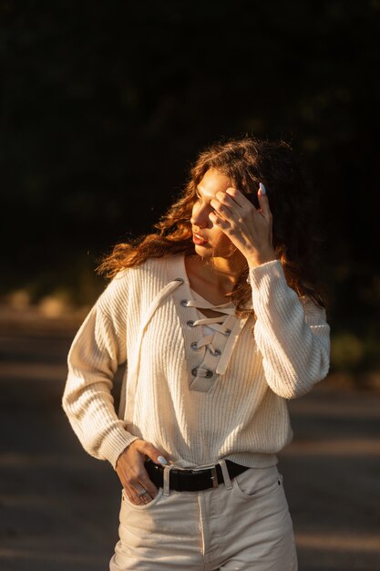 Młoda piękna kręcona kobieta model w bluzie z dzianiny spacery po parku o zachodzie słońca