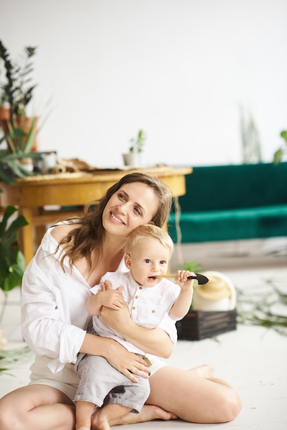 Młoda Piękna Mama Bawi Się Z Dzieckiem Na Podłodze Obok Roślin I Zielonej Sofy