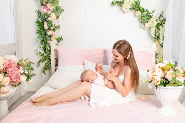 Młoda piękna matka trzyma córkę na białym łóżku, grając i całując ją