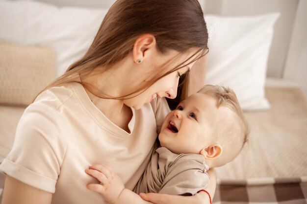 Młoda piękna matka z chłopcem przytulającym się do łóżka w domu w sypialni opieka matki i miłość portret szczęśliwej matki z dzieckiem zdrowe macierzyństwo