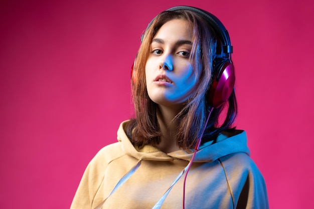 Młoda piękna modna hipster dziewczyna ubrana w bluzę z kapturem, słuchając muzyki w czerwonych słuchawkach w studio czerwonym dramatycznym tle